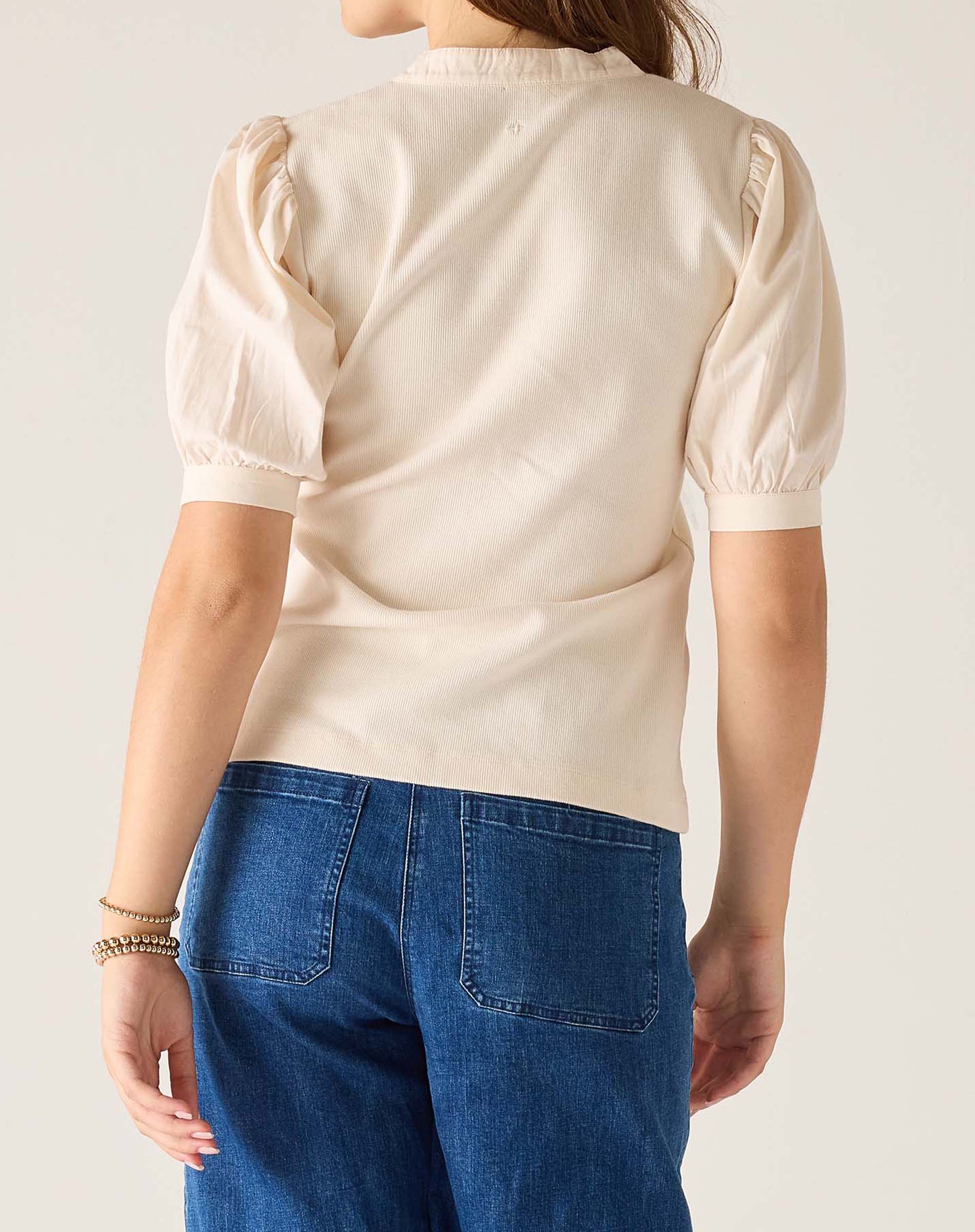 Person wearing a beige blouse with puffed sleeves and blue jeans on a plain background