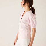 Woman wearing a light pink blouse with sheer sleeves against a white background
