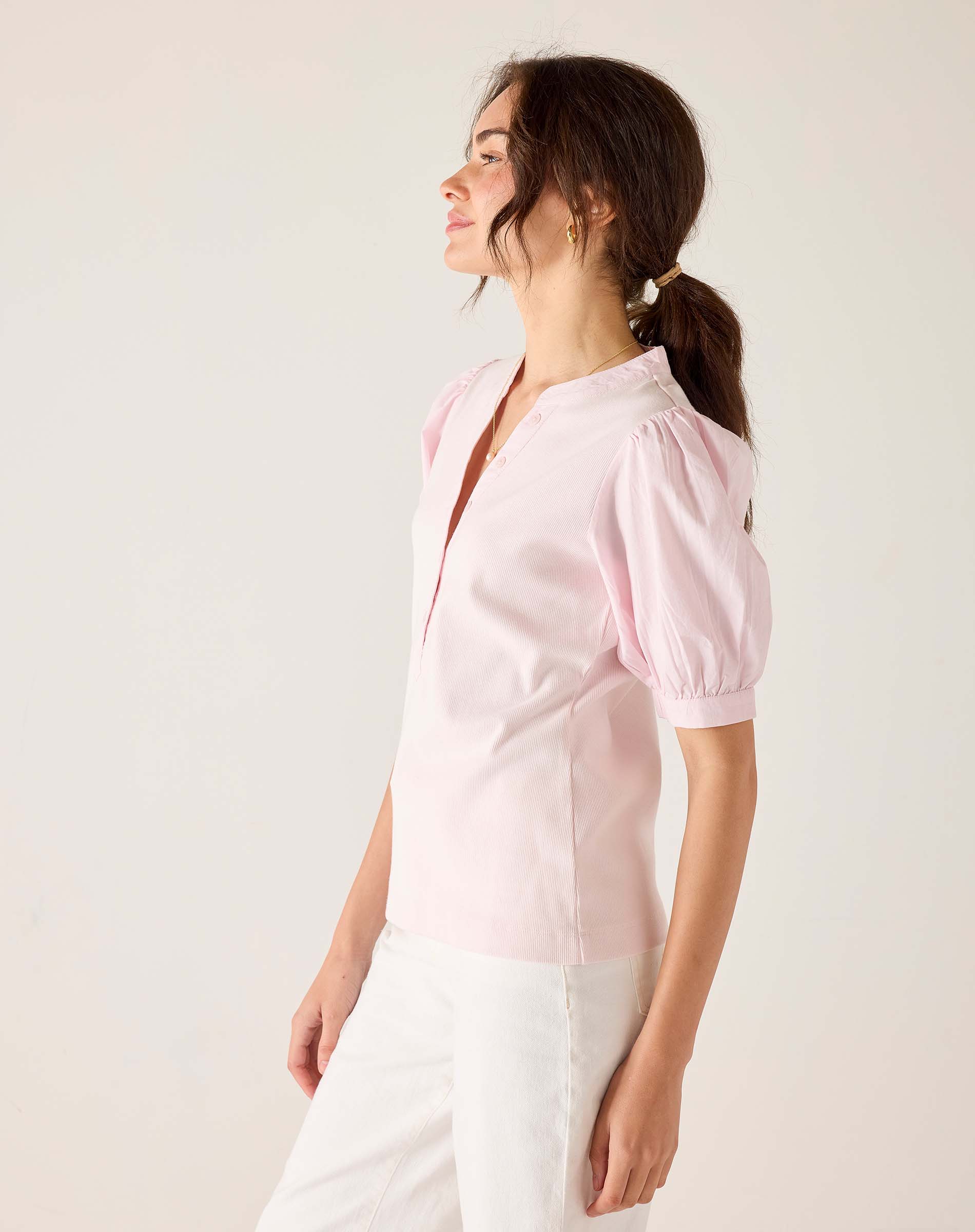 Woman wearing a light pink blouse with sheer sleeves against a white background