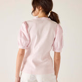 Woman wearing a light pink blouse with puff sleeves against a plain background