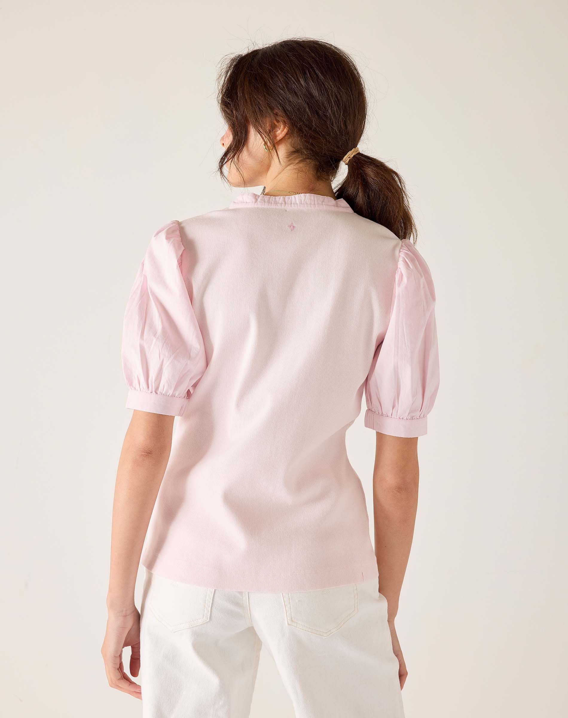 Woman wearing a light pink blouse with puff sleeves against a plain background