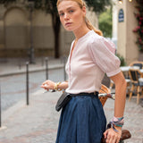 Woman in a white blouse and blue skirt standing on a street with a blurred background