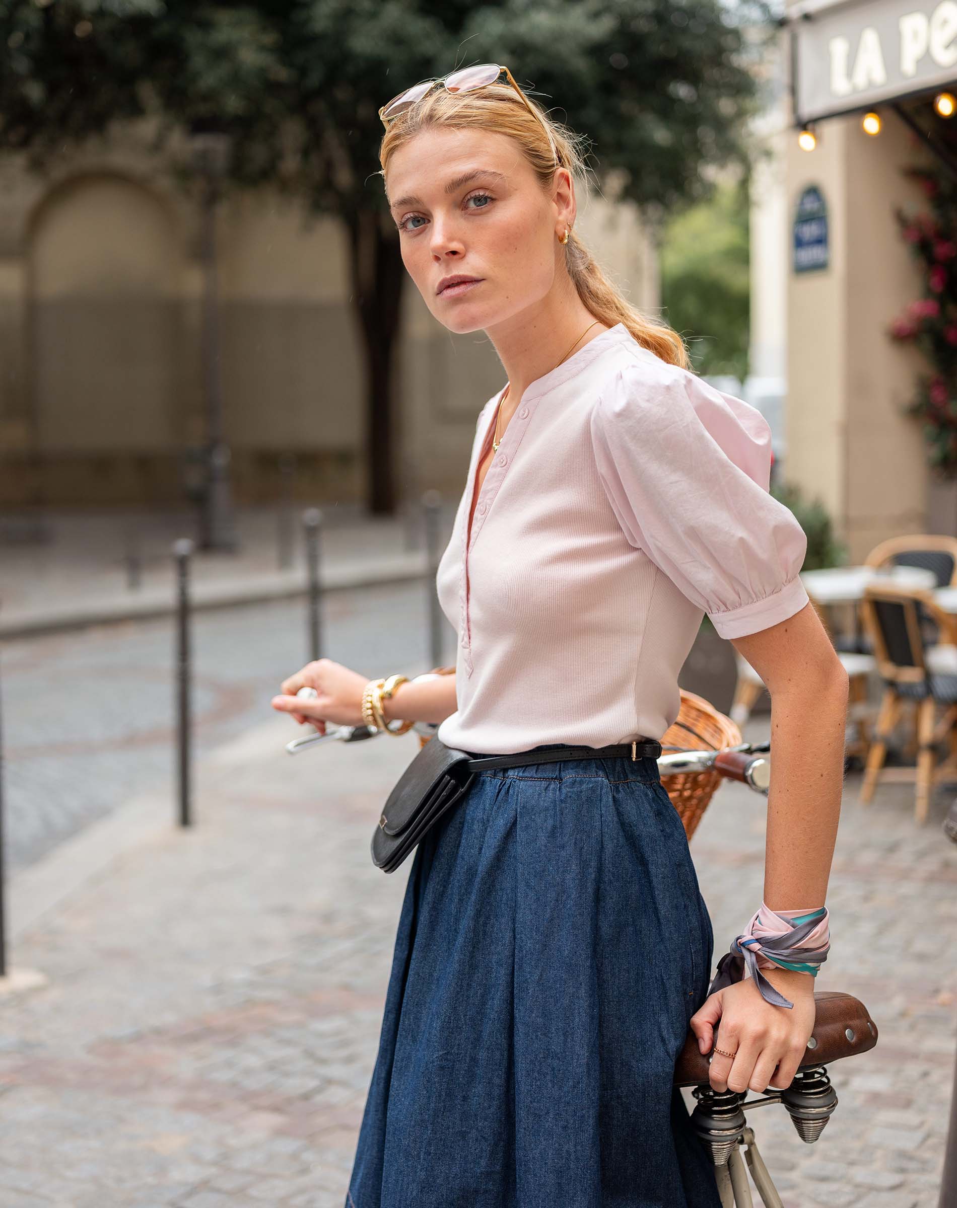 Woman in a white blouse and blue skirt standing on a street with a blurred background