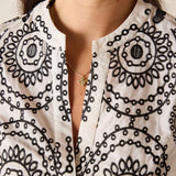 Close-up of a person wearing a white blouse with black circular patterns.