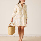 Woman wearing a light-colored dress holding a woven bag against a plain background