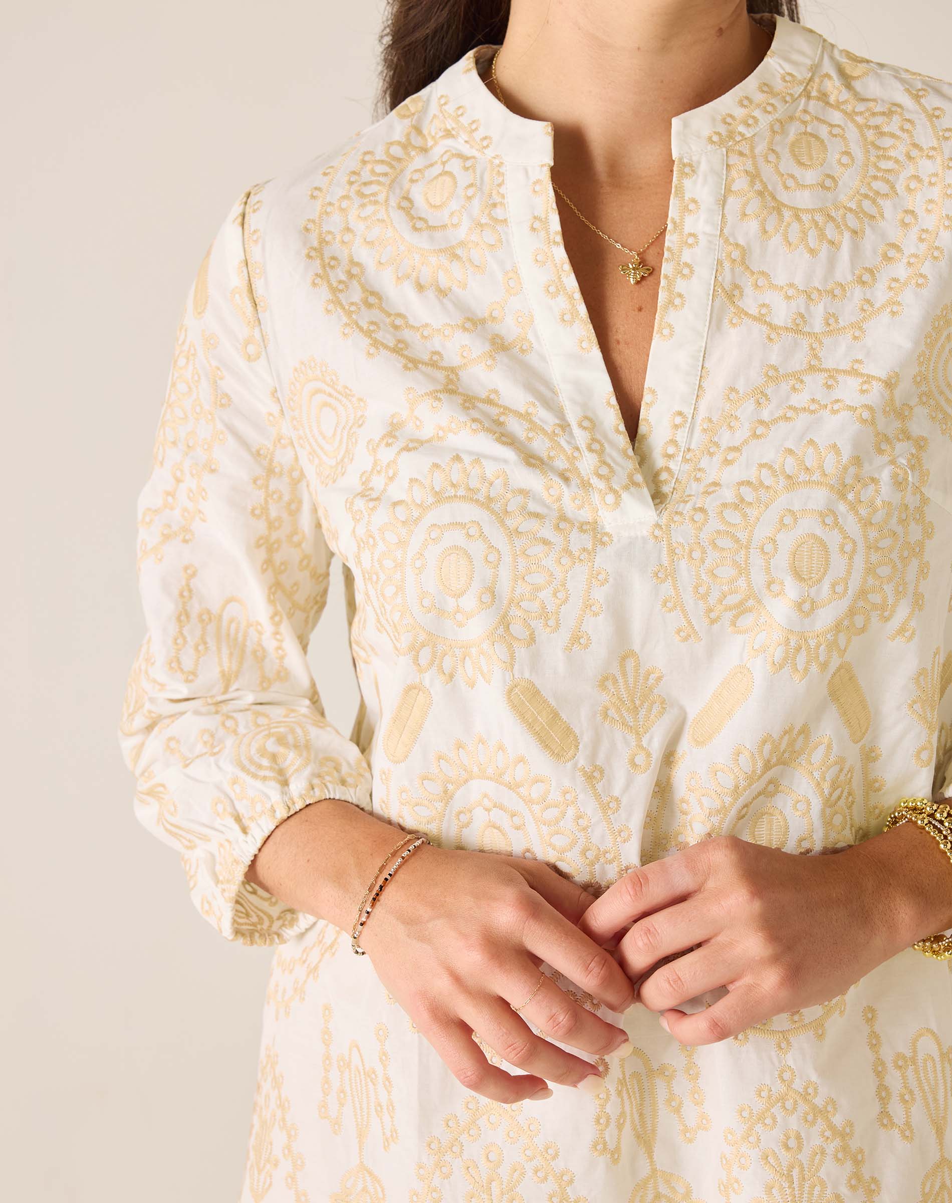 Close-up of a person wearing a white blouse with gold patterns on a plain background