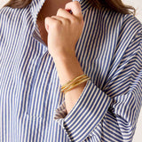 Person wearing a blue and white striped shirt with rolled-up sleeves and gold bracelets.
