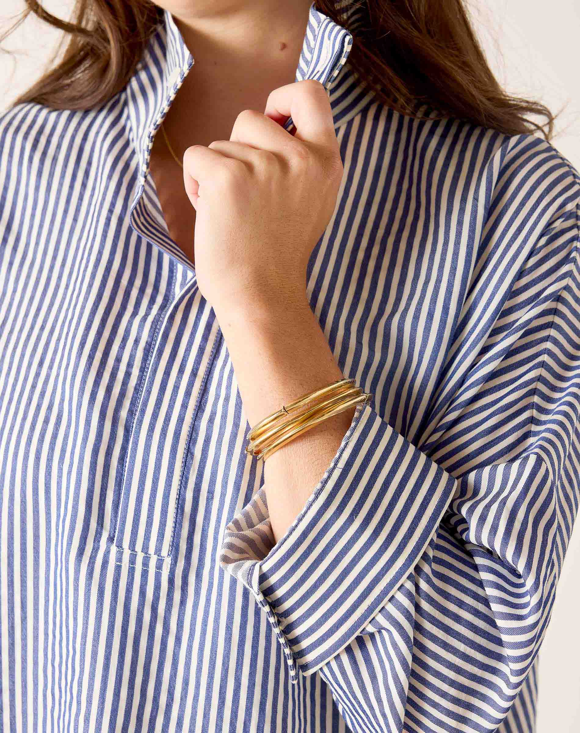 Person wearing a blue and white striped shirt with rolled-up sleeves and gold bracelets.