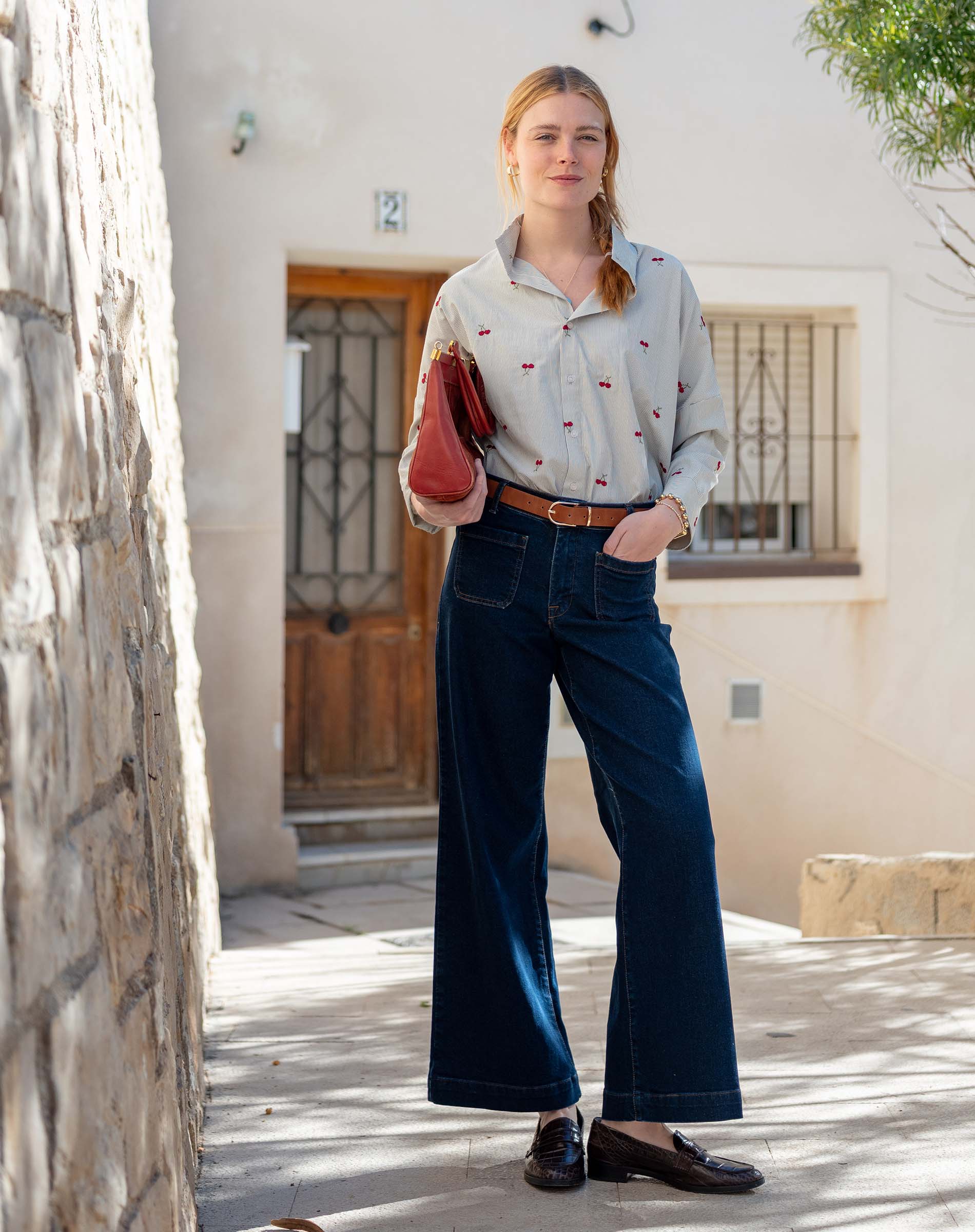 MERSEA ladies' travel-ready light grey shirt with cherry print, worn with high-waisted wide-leg jeans.