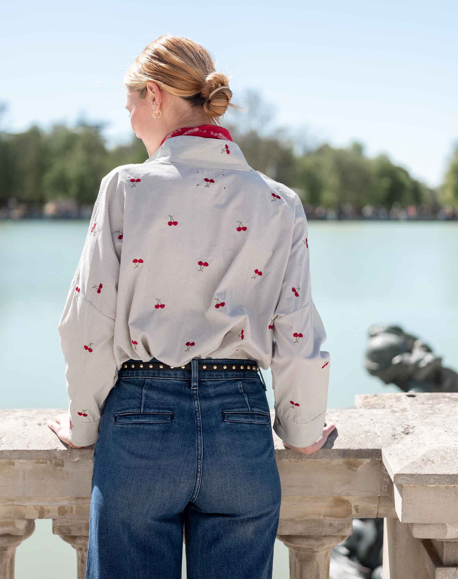 Back view of the light gray button-down shirt with a red cherry print and high-waisted blue denim jeans.