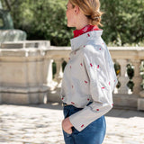 Side view of a white top with red cherries and long sleeves over a red scarf.
