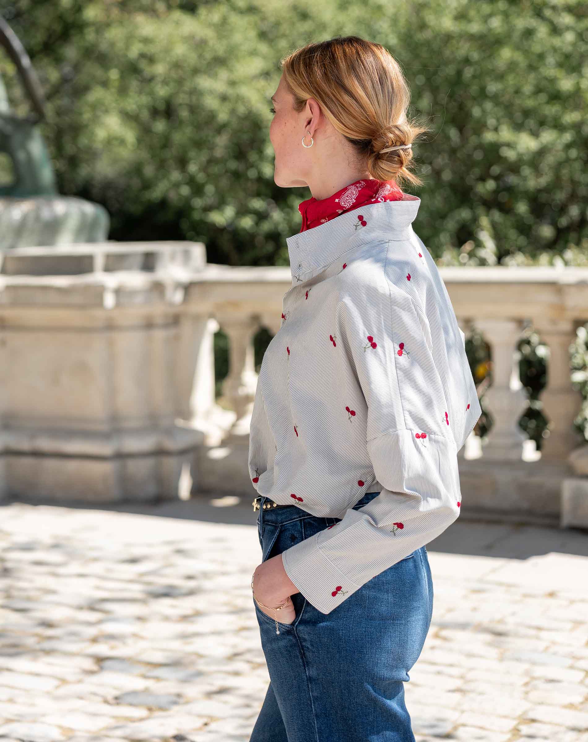 Side view of a white top with red cherries and long sleeves over a red scarf.