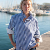 Blue double stripe shirt with an Elizabethan collar and rolled sleeves set in a harbor scene.