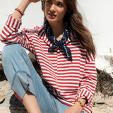 Woman wearing a red and white striped shirt with a blue scarf, sitting outdoors.