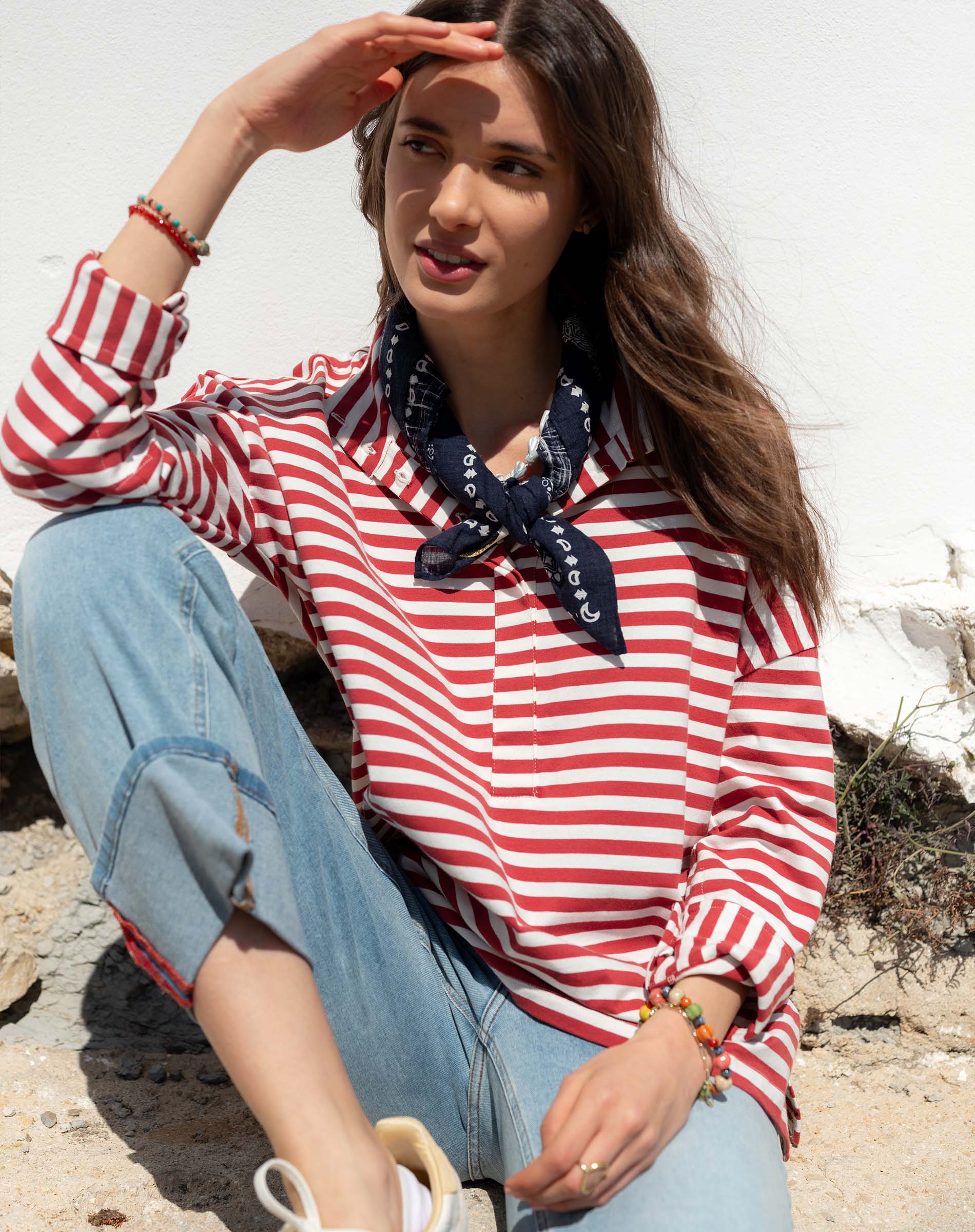 Woman wearing a red and white striped shirt with a blue scarf, sitting outdoors.