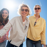 Three women standing together outdoors with a clear blue sky.