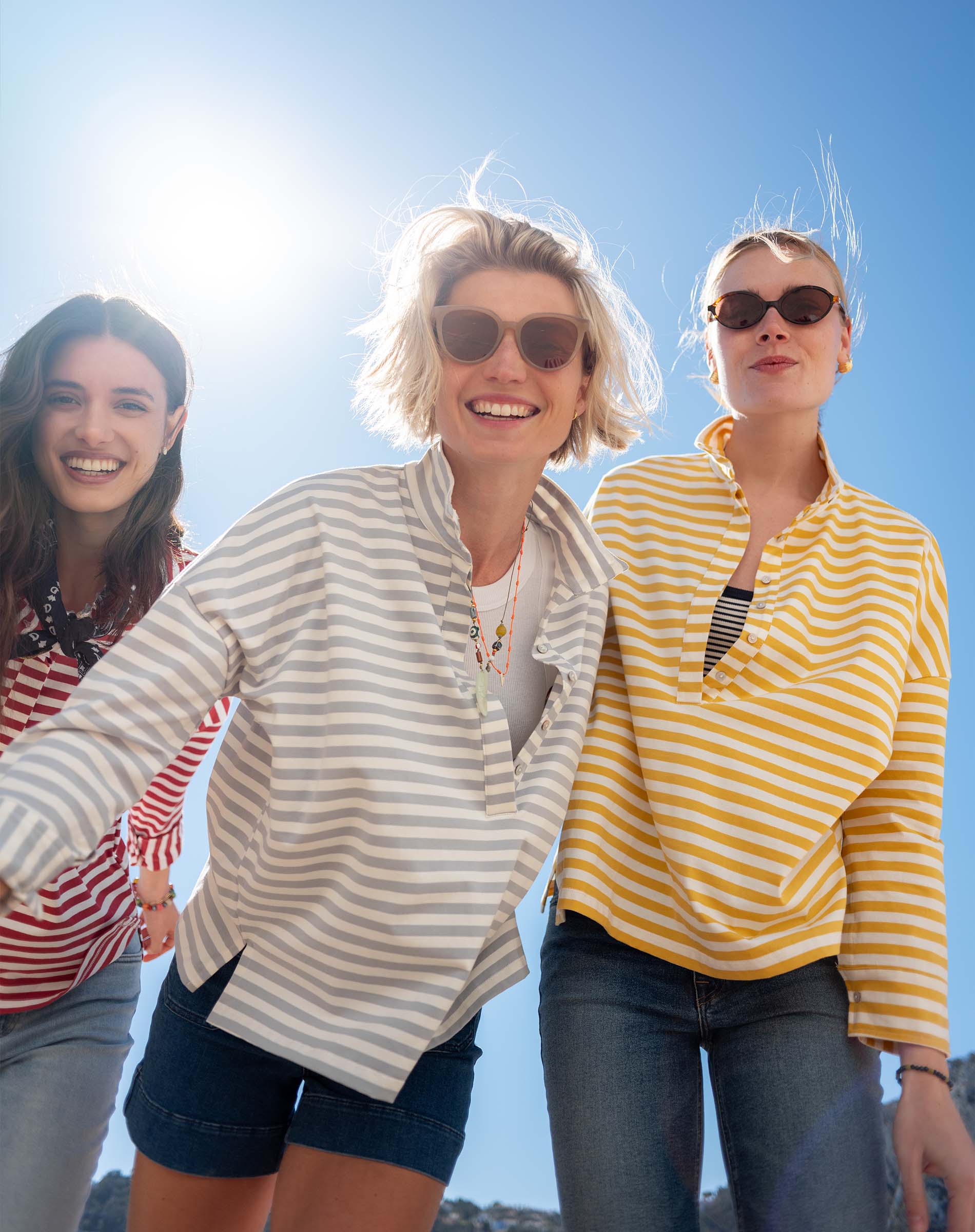 MERSEA women's travel-friendly golden rod striped pop-up collar knit top worn by two models in a coastal beach setting.