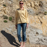 Person wearing a yellow striped shirt and blue jeans standing on a rocky beach.