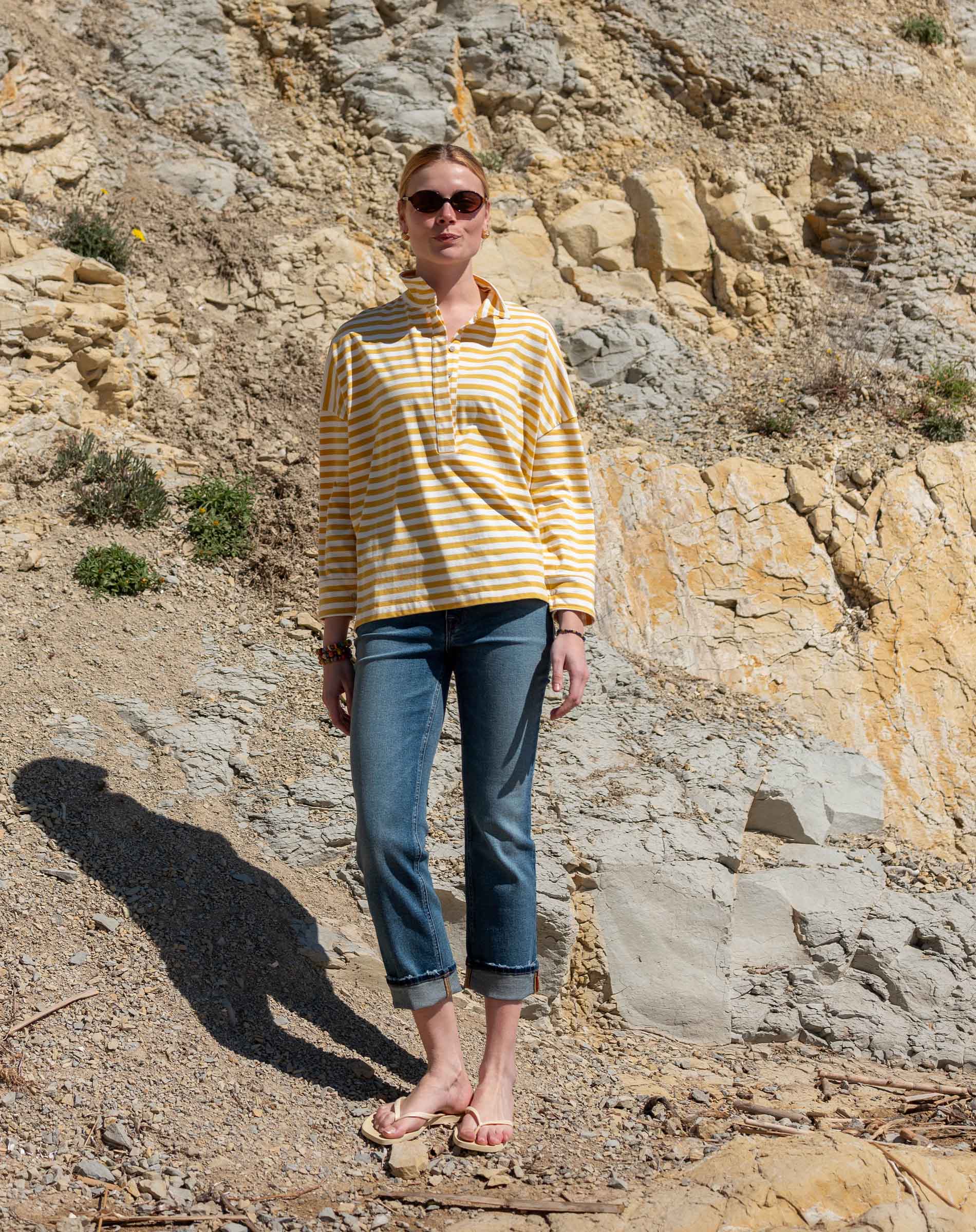 Person wearing a yellow striped shirt and blue jeans standing on a rocky beach.