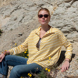 Woman in a yellow and white striped shirt sitting on rocky terrain with wildflowers.