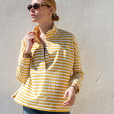 Woman wearing a yellow and white striped shirt against a light gray wall.