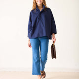 Woman wearing a navy jacket and blue jeans holding a brown leather bag on a white background