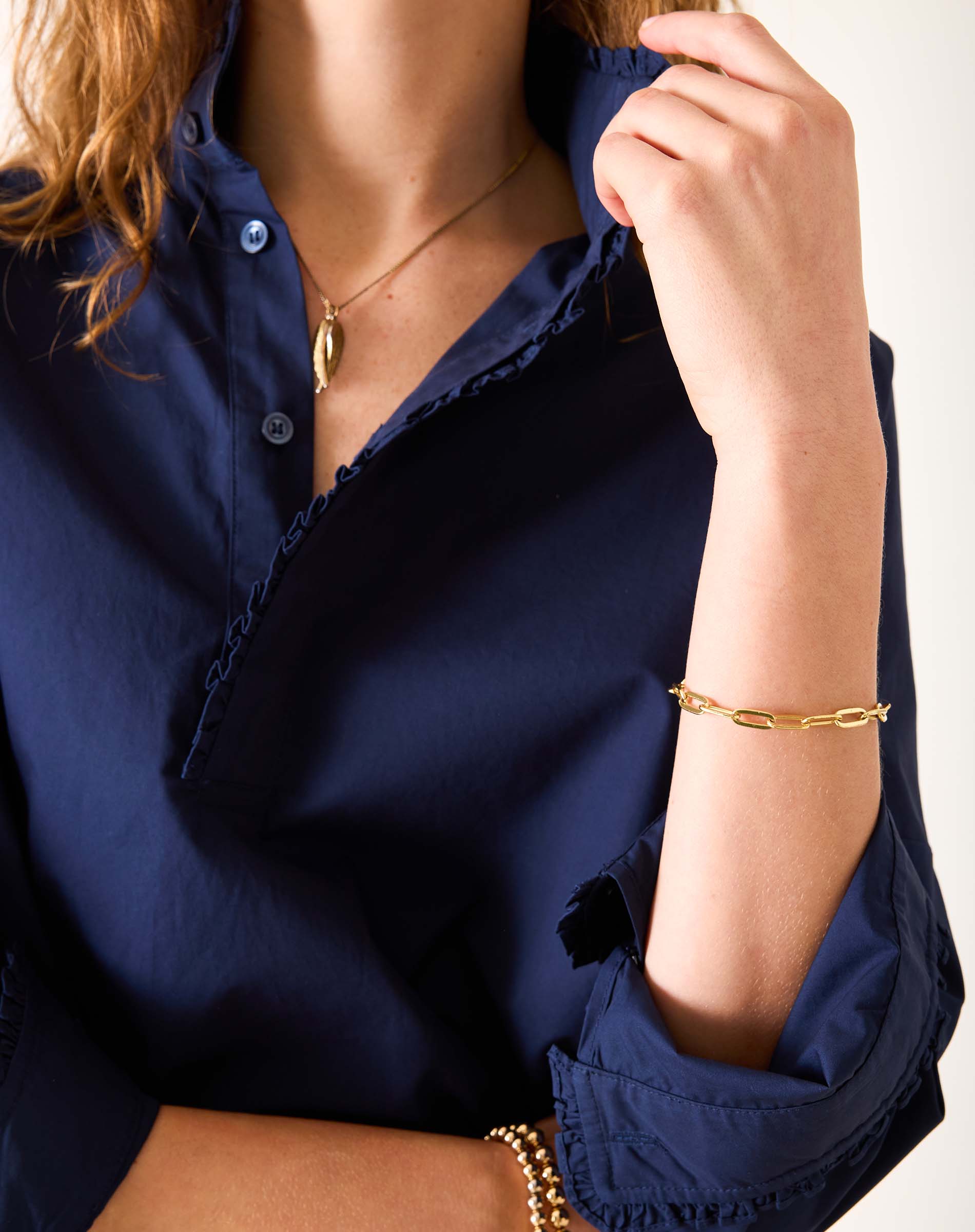 Person wearing a navy blue shirt with gold jewelry on a white background
