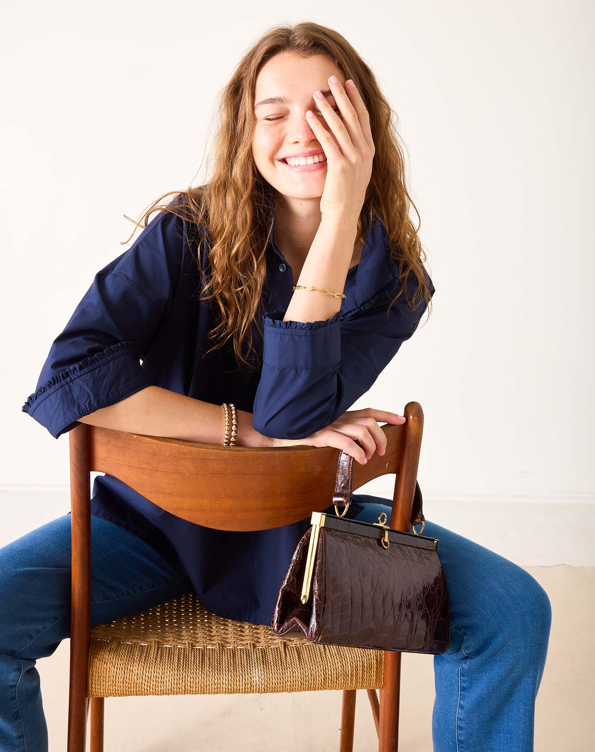 Woman sitting on a chair with a handbag next to her, smiling.
