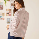 Woman wearing a striped shirt in a room with a white wall and decorative elements.