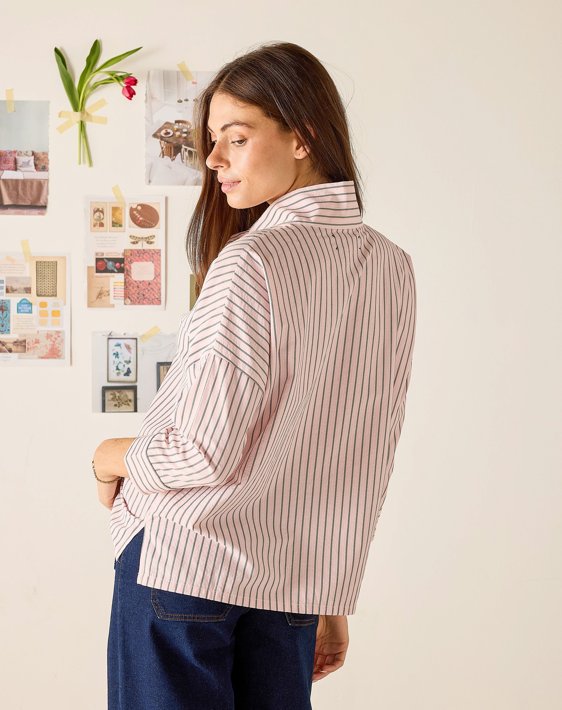 Woman wearing a striped shirt in a room with a white wall and decorative elements.