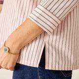 Person wearing a pink and white striped shirt with rolled-up sleeves and blue jeans.