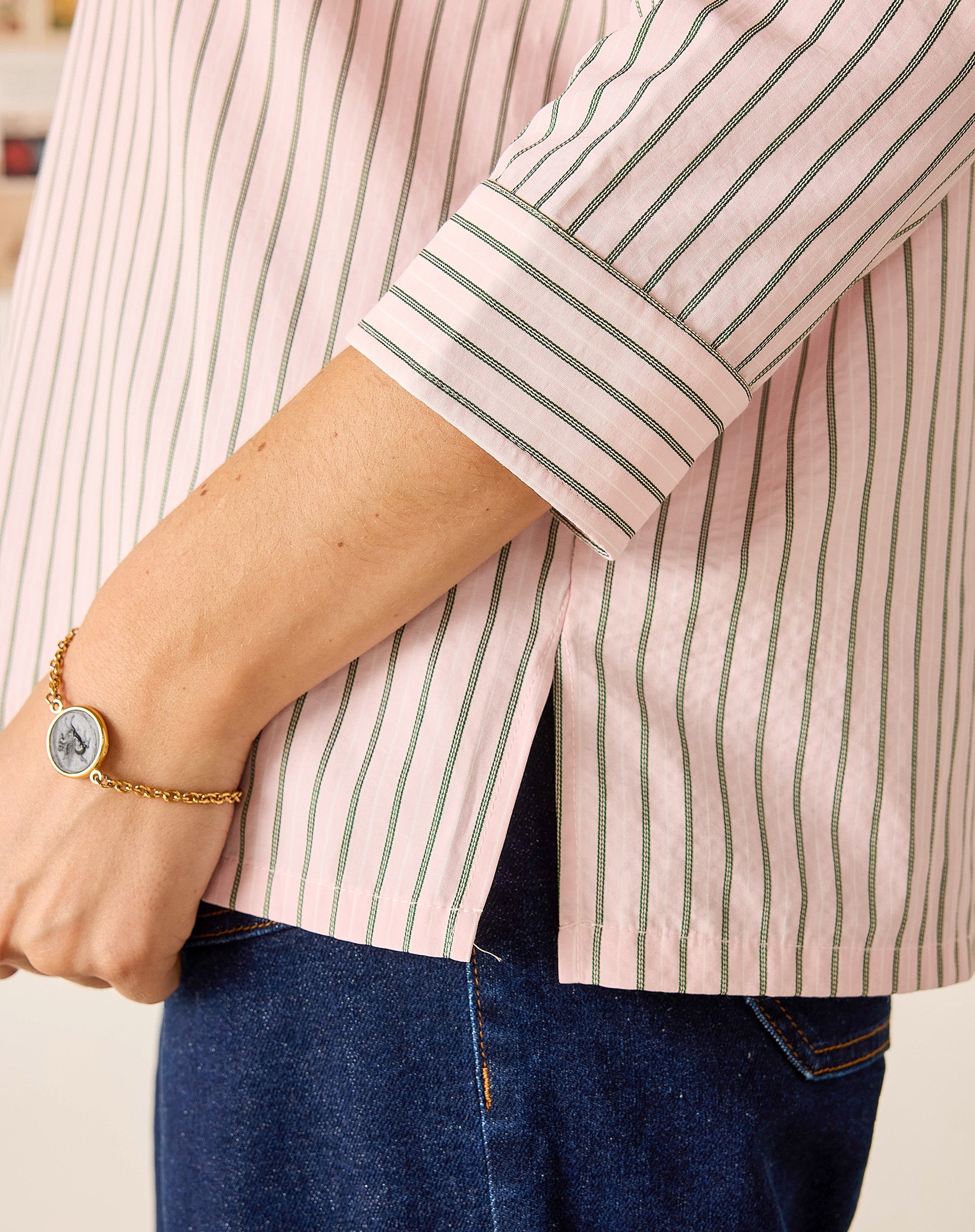 Person wearing a pink and white striped shirt with rolled-up sleeves and blue jeans.
