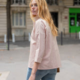 Woman wearing a light pink ribbed sweater and blue jeans on a city street.