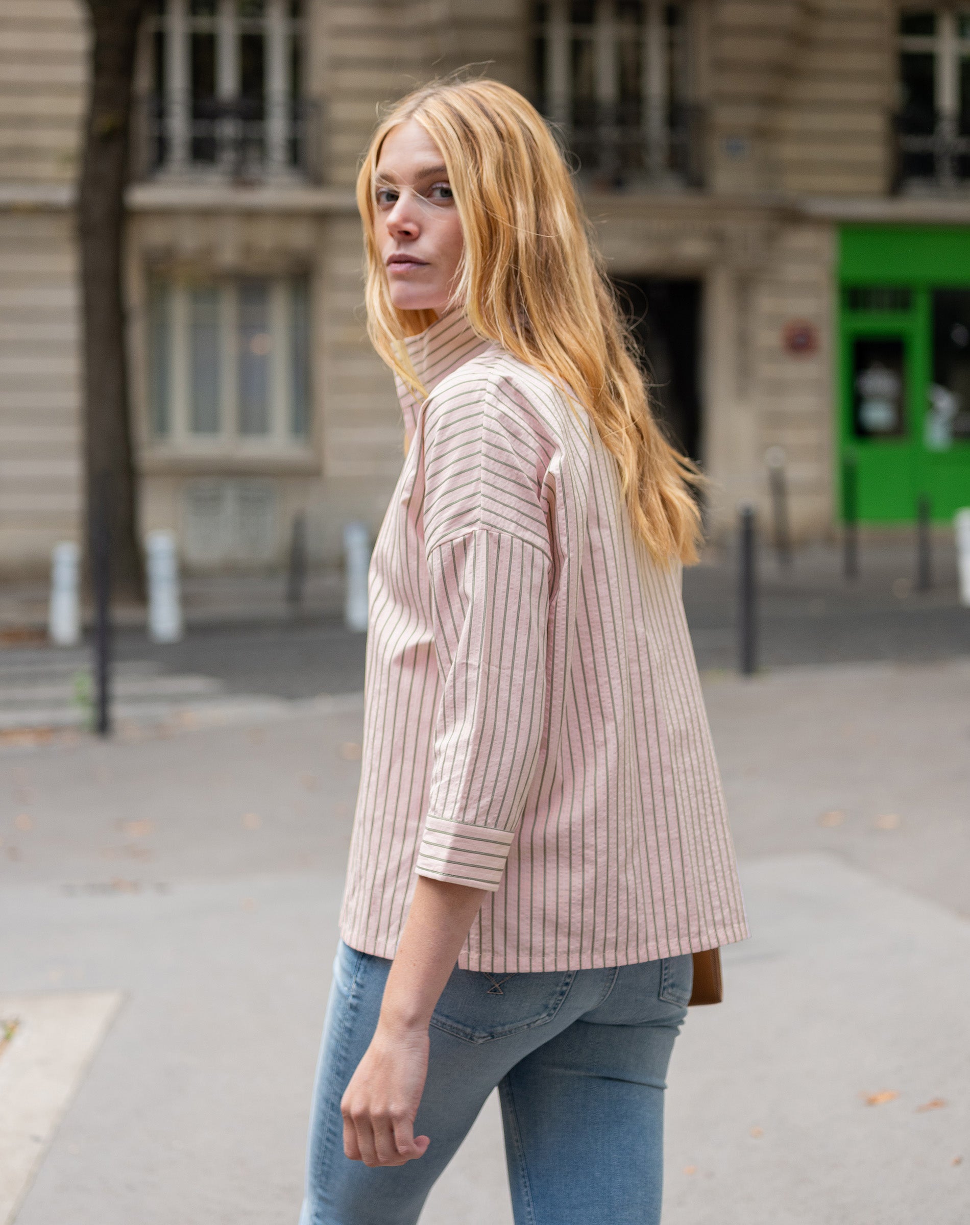 Woman wearing a light pink ribbed sweater and blue jeans on a city street.