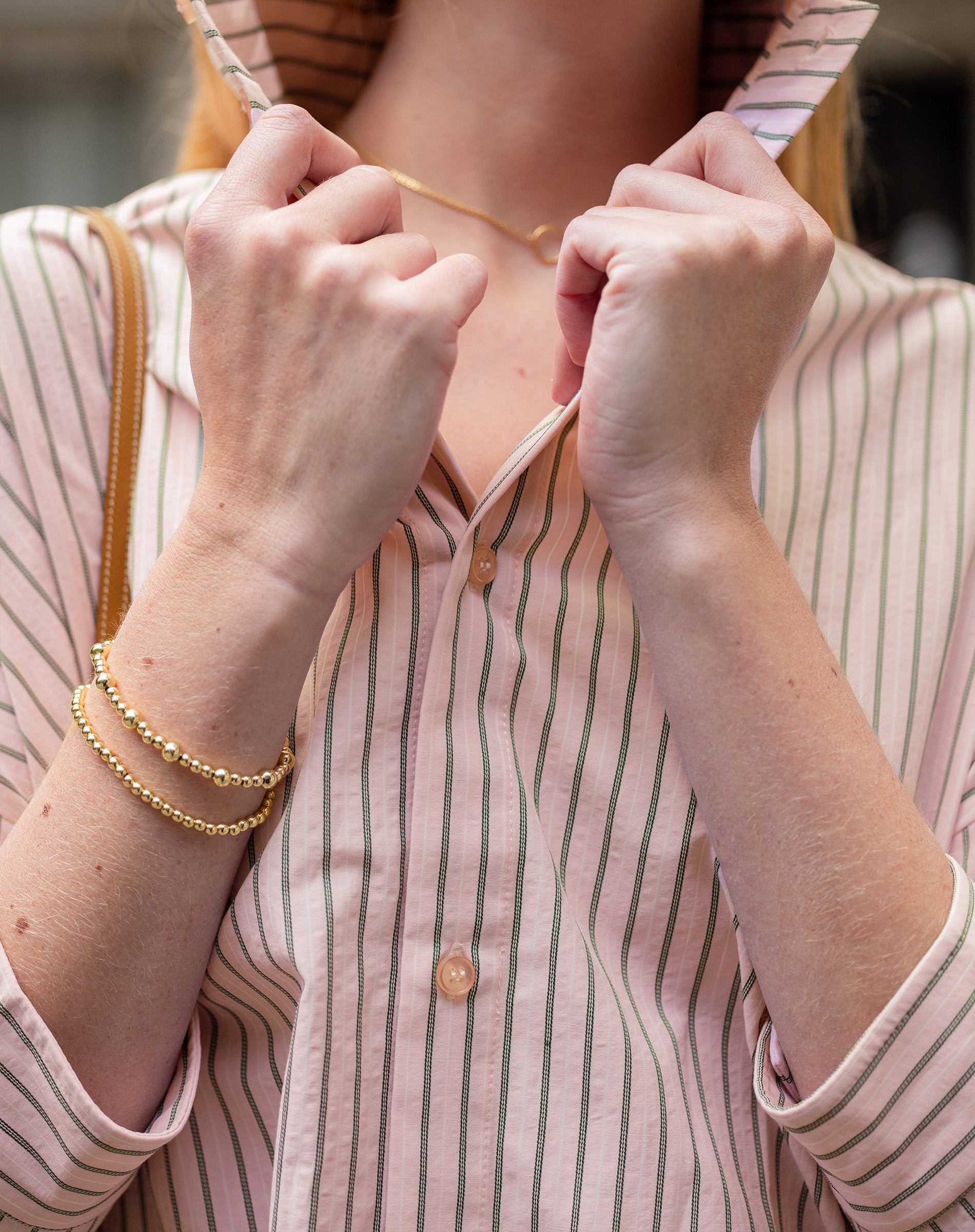Close-up of a person wearing a striped shirt with a focus on their hands and jewelry.