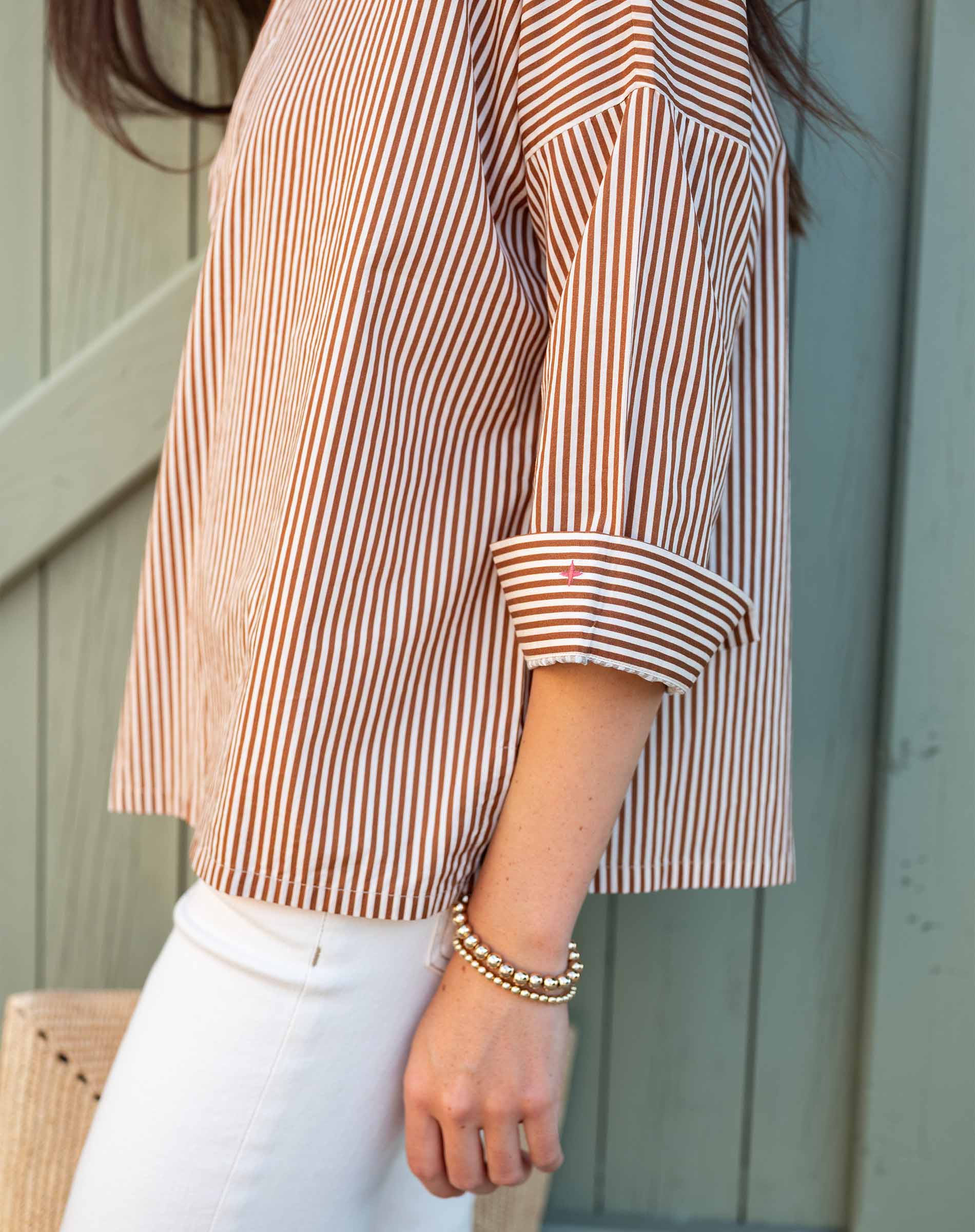 Person wearing a striped shirt and white pants with a neutral background