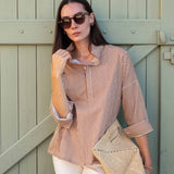 Woman in a striped shirt and sunglasses holding a beige bag against a wooden background