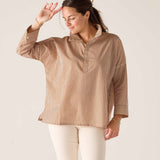 Woman wearing a brown striped shirt and white pants against a plain background