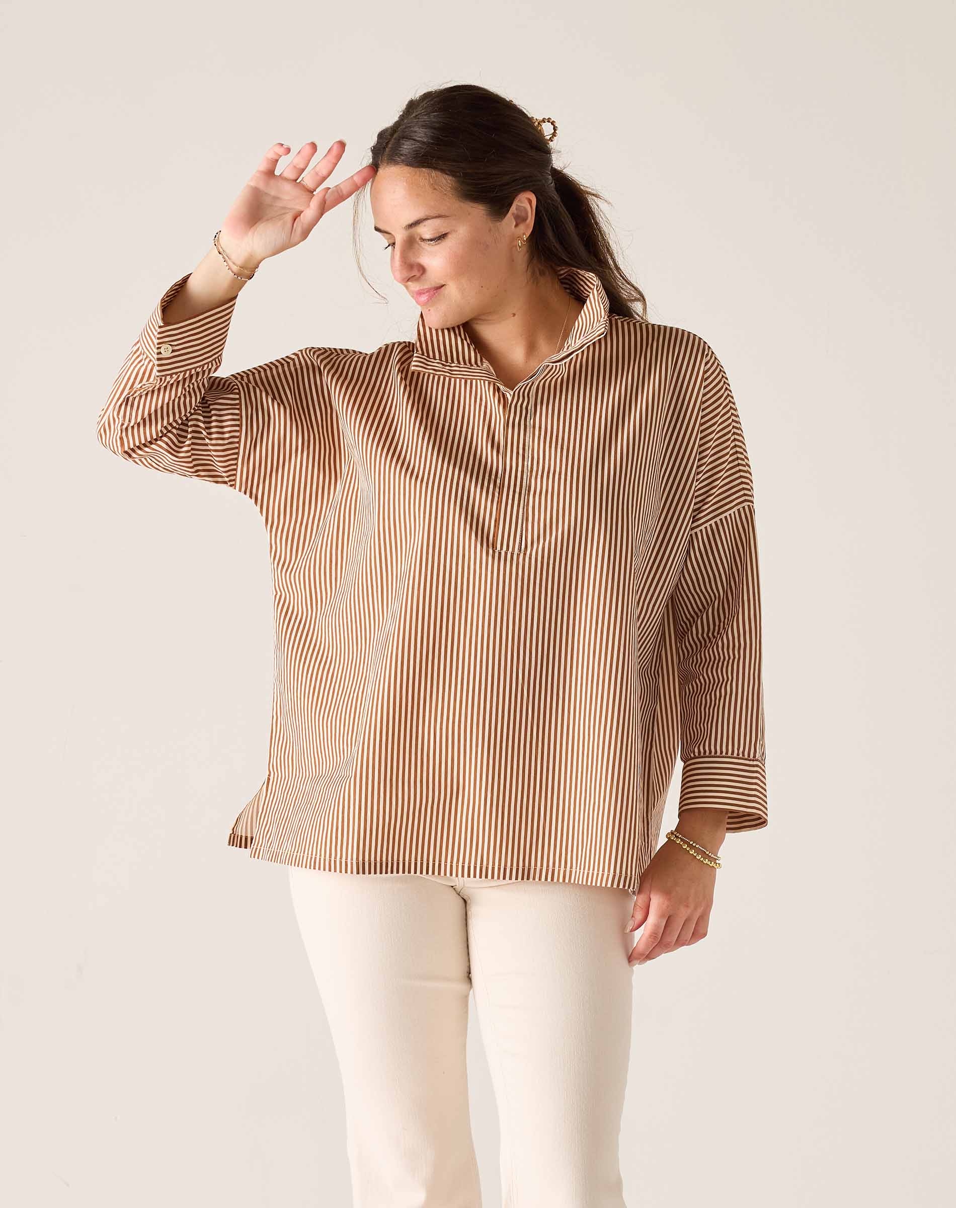 Woman wearing a brown striped shirt and white pants against a plain background