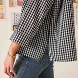 Person wearing a black and white checkered shirt and blue jeans against a light background
