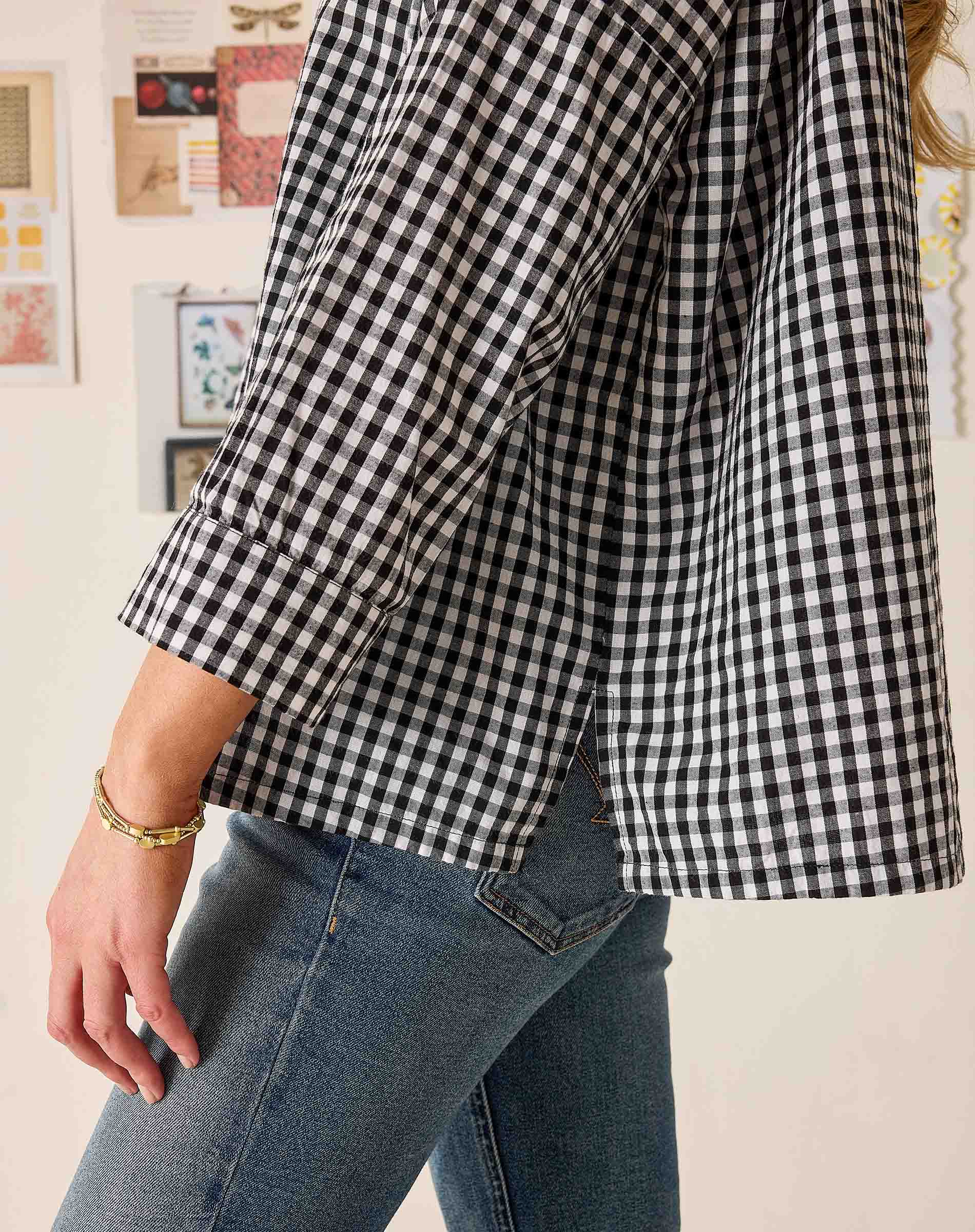Person wearing a black and white checkered shirt and blue jeans against a light background