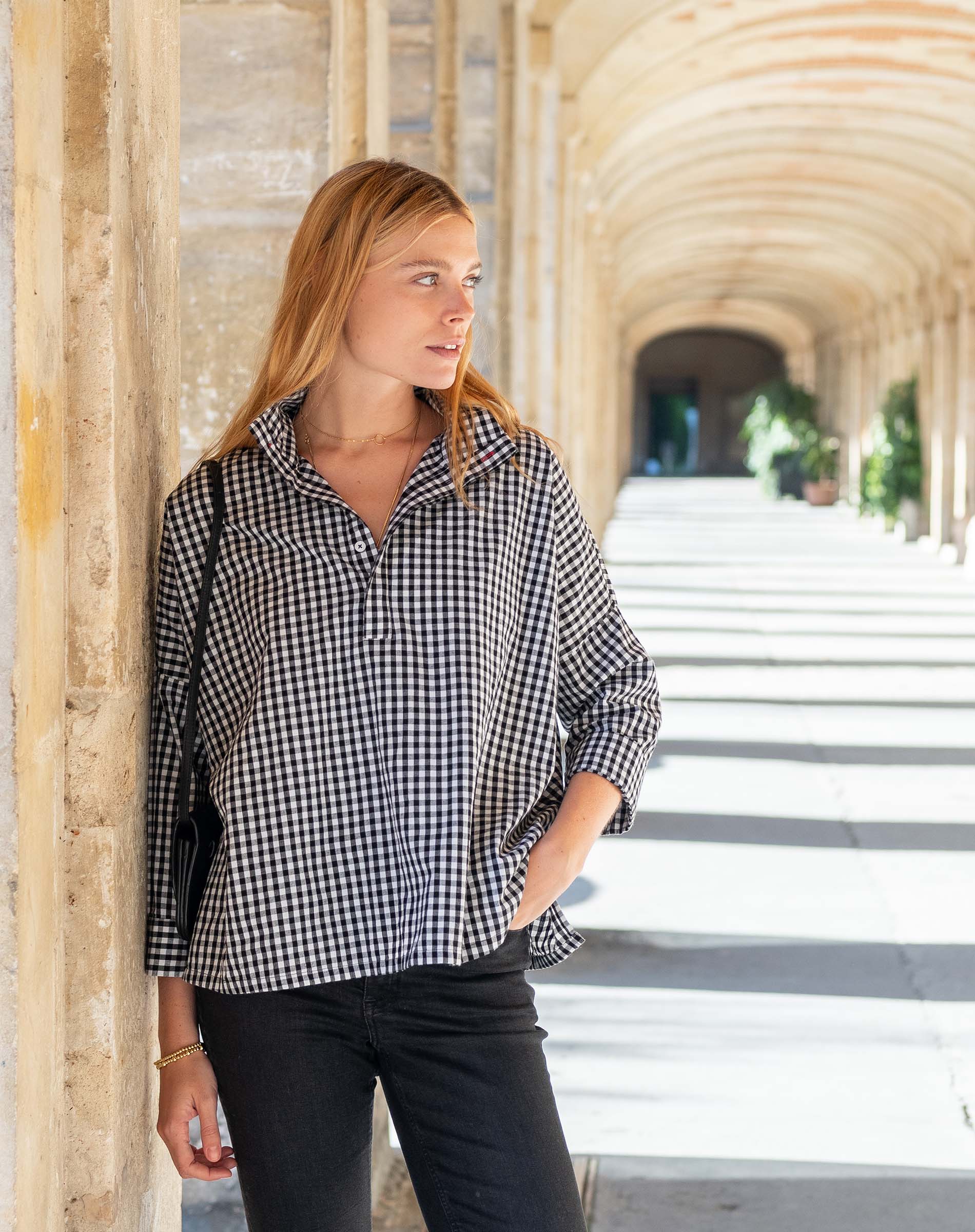 Woman wearing a black and white checkered shirt standing in an architectural setting.