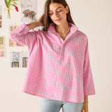 Woman wearing a pink checkered shirt in a room with framed pictures on the wall.