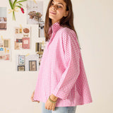 Woman wearing a pink checkered shirt standing in front of a wall with decorative items.