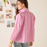Woman wearing a pink checkered shirt in a room with decorative elements on the wall.