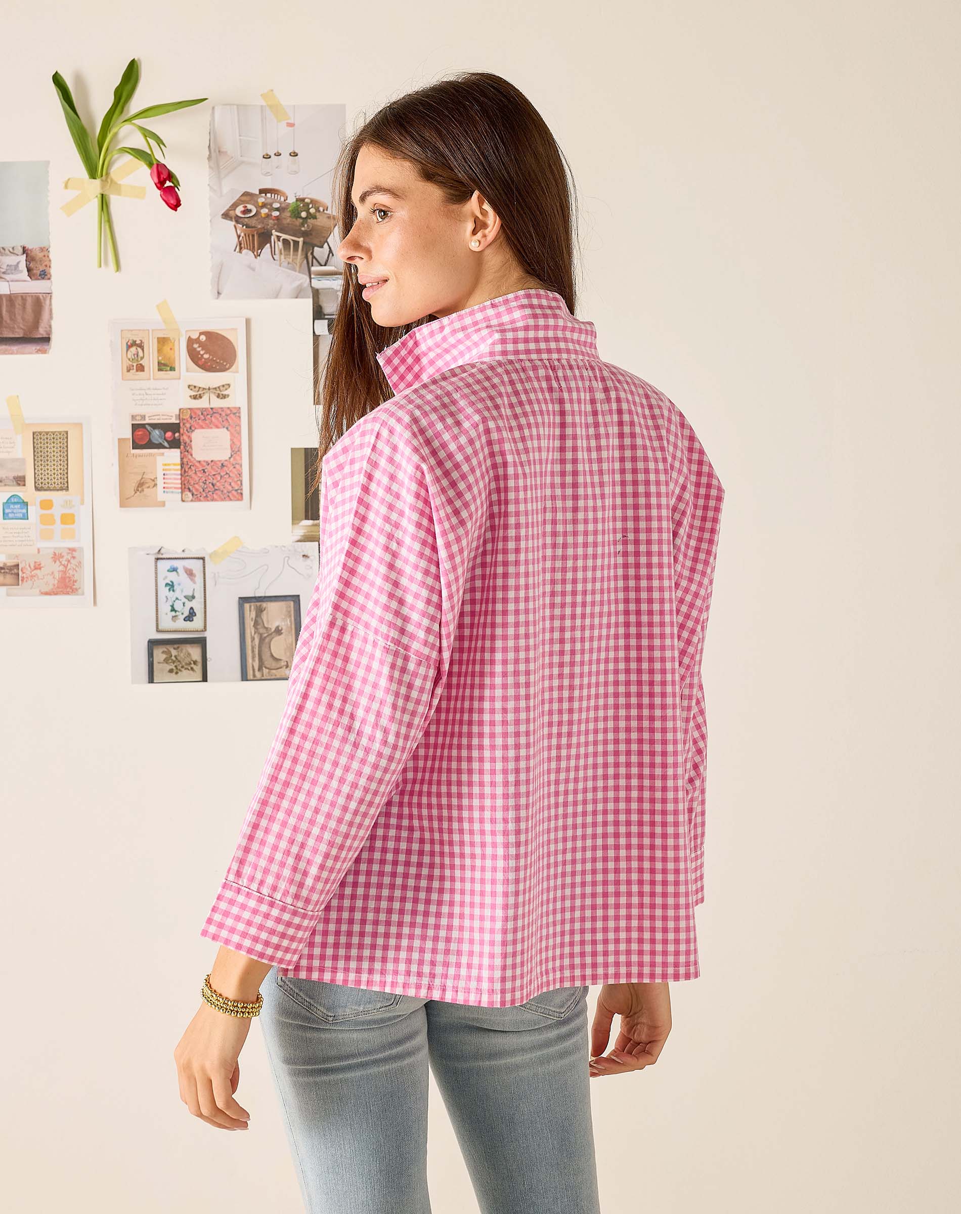 Woman wearing a pink checkered shirt in a room with decorative elements on the wall.