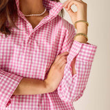 Person wearing a pink gingham shirt with rolled-up sleeves on a beige background