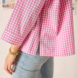 Person wearing a pink and white checkered shirt with light blue jeans against a neutral background