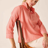 Woman wearing a red and white striped shirt sitting on a wooden chair with a beige cushion.