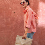 Woman holding a woven bag against a pink wall